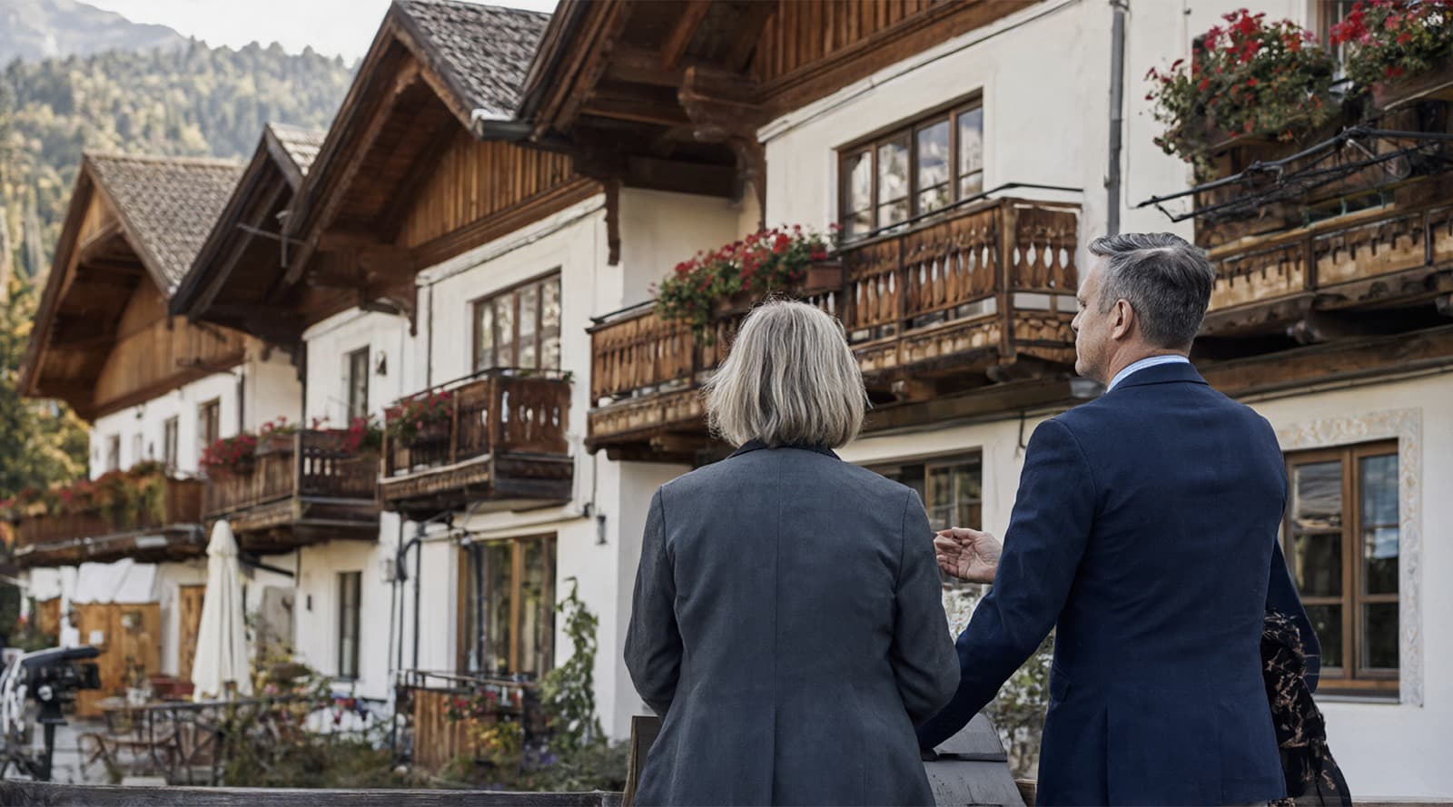 Zwei Personen betrachten ein traditionelles Alpenhotel mit Holzbalkonen